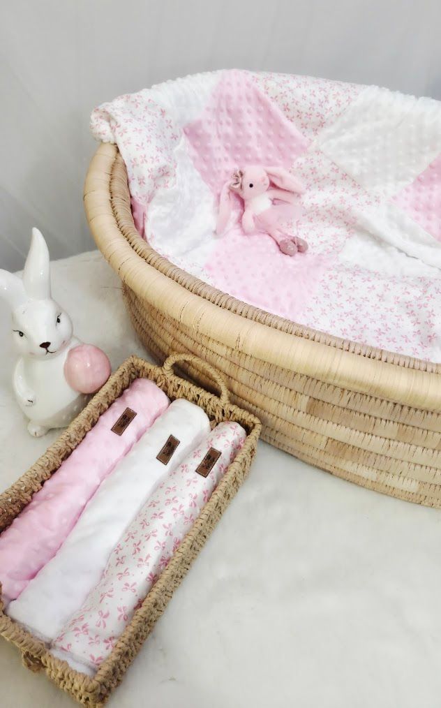 Pink baby Moses basket with floral blanket, stuffed bunny toy, white ceramic rabbit figurine, and folded swaddle cloths in wicker basket.