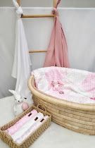Pink and white baby Moses basket with soft blankets, a plush bunny toy, and a decorative ladder in a nursery.