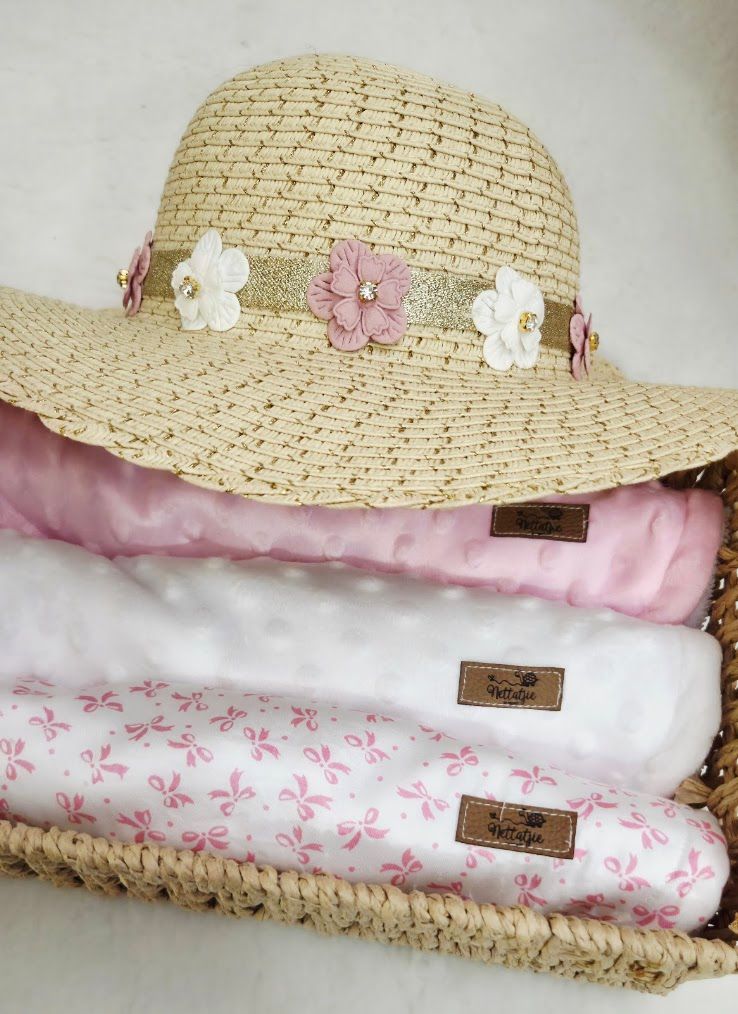 Straw sun hat with pink and white floral trim displayed on a basket with folded pink and white blankets.