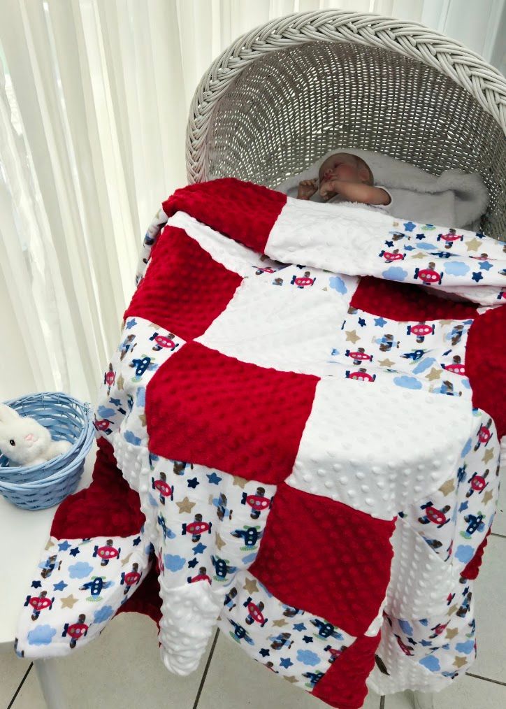 Baby sleeping in wicker bassinet covered with red and white patchwork minky quilt featuring airplane print fabric.