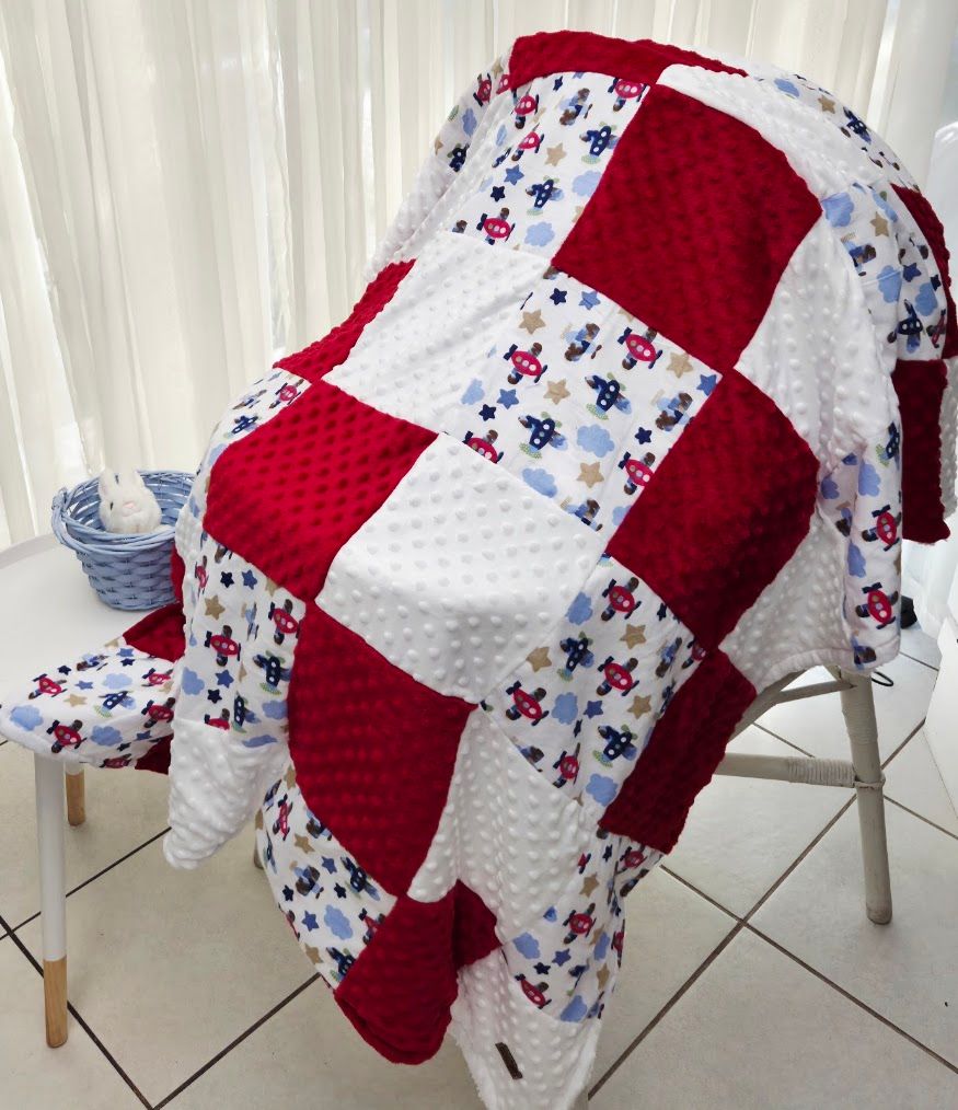 Red and white patchwork baby quilt with airplane print squares draped over a chair.