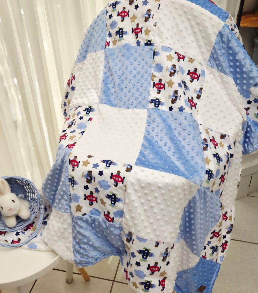 Blue patchwork baby quilt with airplane and star prints, minky dot fabric squares, displayed on a chair.