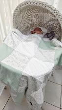 Newborn baby sleeping peacefully in a wicker bassinet with a soft mint and white patchwork blanket.