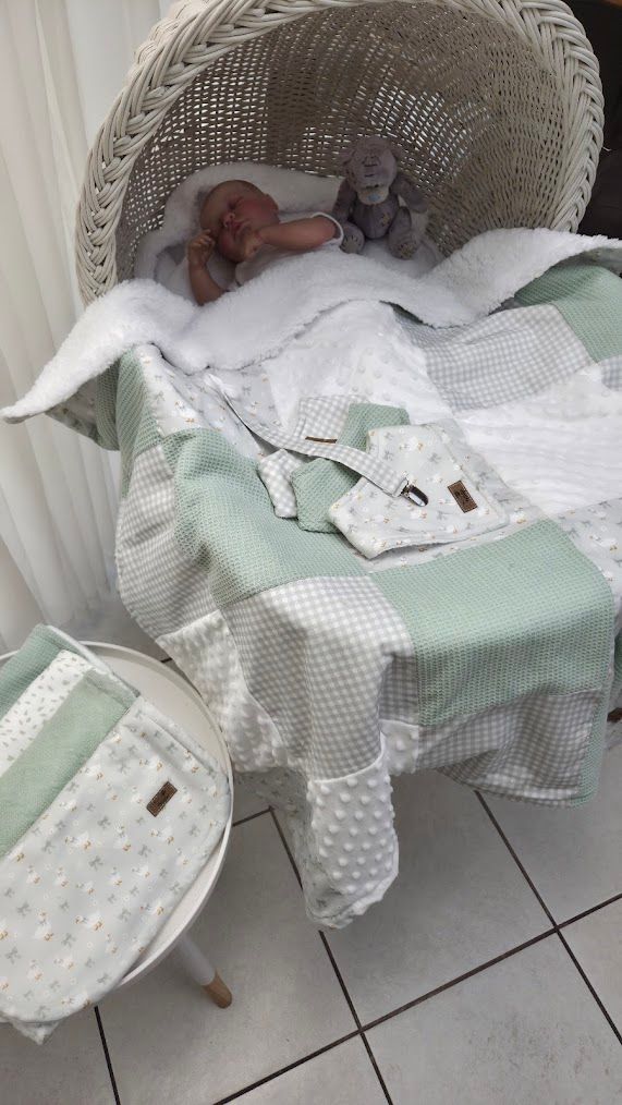 Sleeping newborn baby in white wicker bassinet with mint green patchwork blanket and matching diaper bag set.