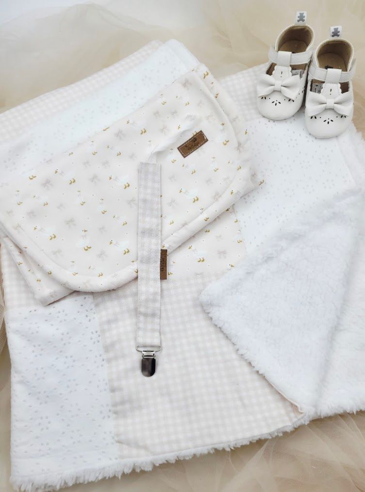 White baby gift set with floral burp cloth, gingham pacifier clip, eyelet blanket, and white leather shoes.
