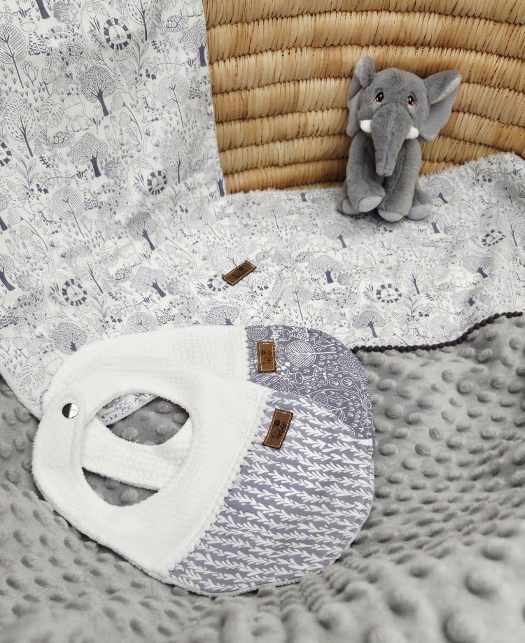 Gray knit baby sleep sack with white minky dot blanket, elephant plush toy, and woodland print swaddle on soft bedding.