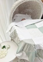 Newborn baby resting in a white wicker Moses basket with sage green and white patchwork quilt blanket.