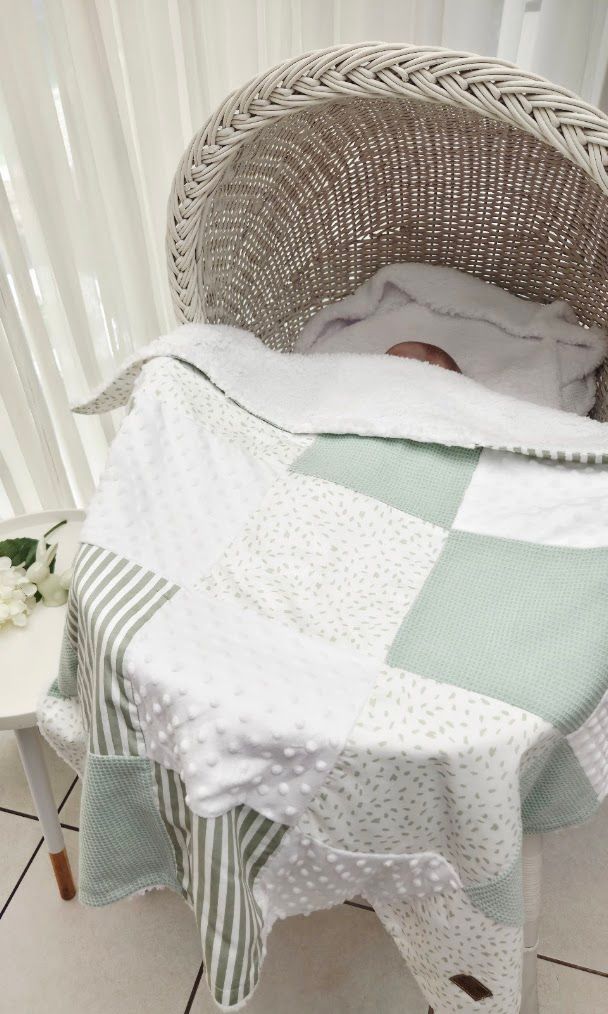 Baby resting in a wicker bassinet covered with a patchwork quilt in mint green, white, and sage stripes.
