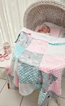 Baby sleeping in wicker bassinet with pink and mint patchwork quilt blanket, soft nursery decor.