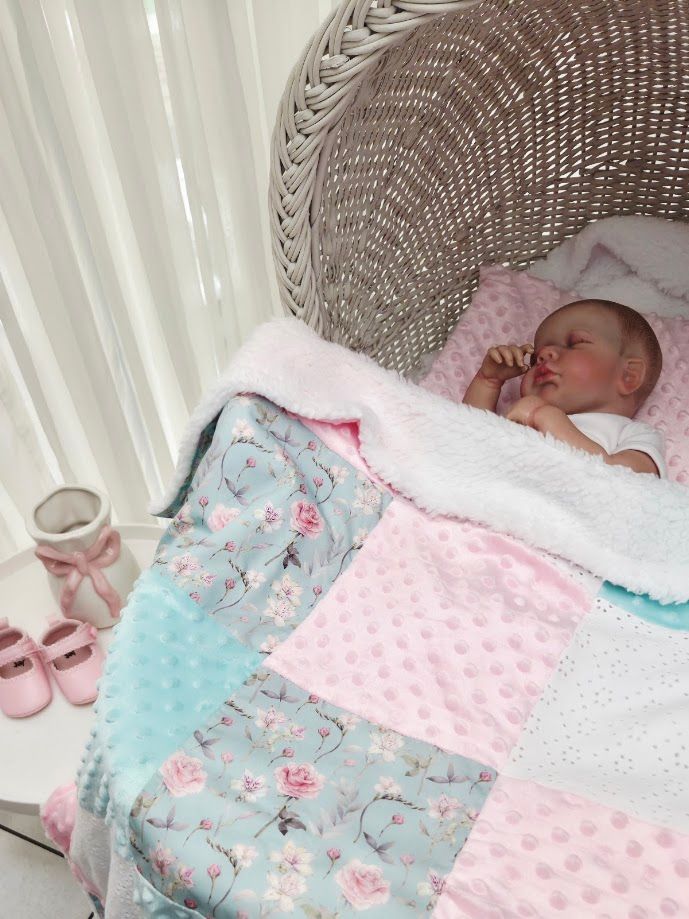 Sleeping newborn baby in wicker chair with pink floral patchwork quilt and pink shoes.