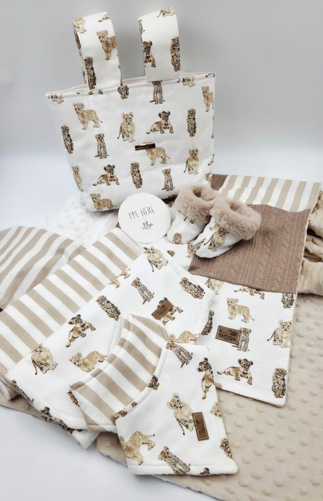 Neutral-toned baby gift set featuring dog-print fabric items, striped blanket, booties, and textured accessories.