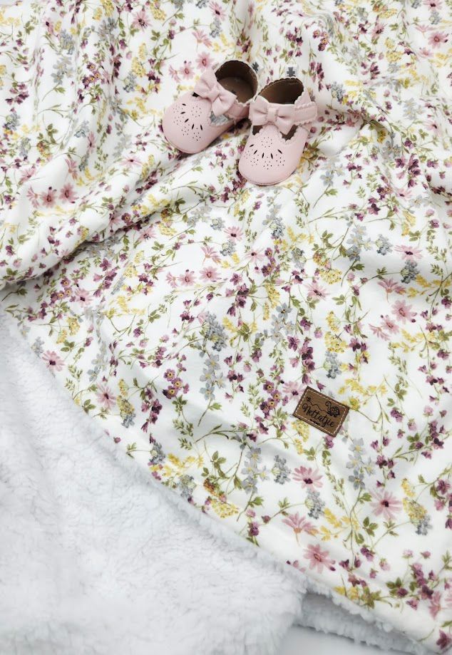 Floral baby blanket with pink bow shoes on white sherpa, featuring delicate wildflower print in pink and yellow.