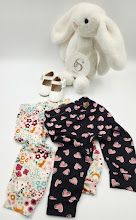 White plush bunny toy with two pairs of baby leggings, floral print and pink hearts, plus tiny shoes.