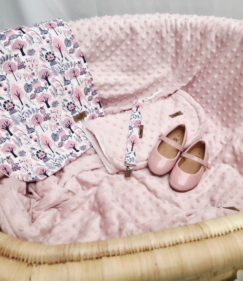 Pink baby bassinet with floral patterned blanket, soft pink minky blanket, pacifier clip, and pink Mary Jane baby shoes.
