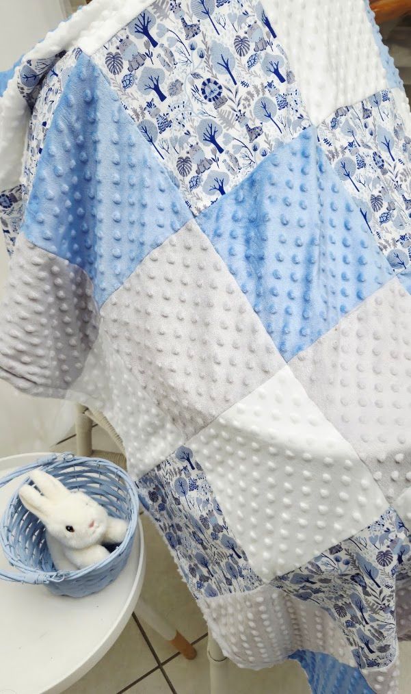 Blue and white patchwork baby quilt with minky dot fabric draped over a chair, with a small bunny toy in a basket.