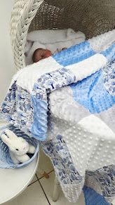 Blue and white patchwork baby blanket with minky dots draped over a wicker chair with sleeping newborn.