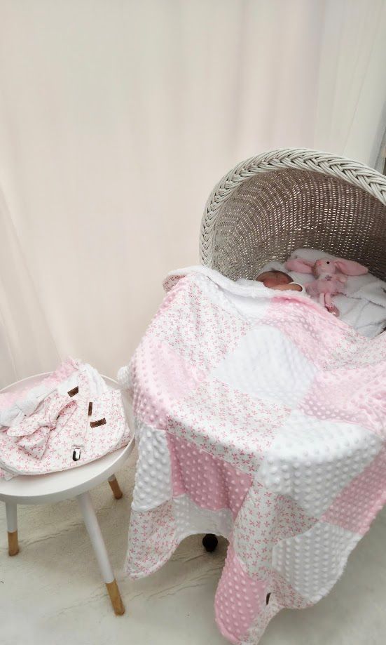 Sleeping newborn baby in a white wicker Moses basket covered with a pink and white patchwork minky blanket.