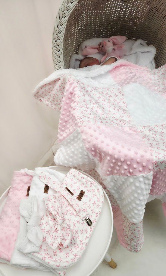 Newborn baby wrapped in pink and white minky dot blanket resting in a wicker bassinet with matching accessories.