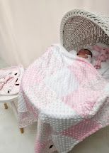 Baby sleeping in a wicker bassinet covered with a soft pink and white patchwork minky blanket.