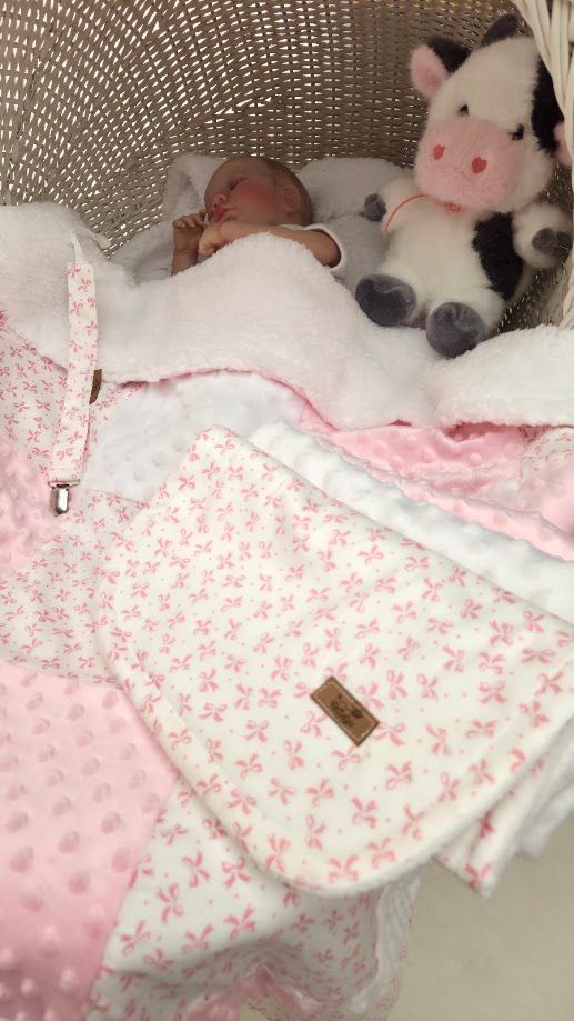 Newborn baby sleeping in wicker bassinet with pink floral blanket beside a stuffed cow toy.