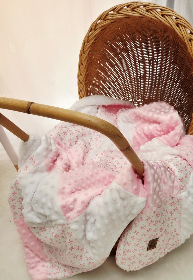 Pink floral and minky dot baby blanket draped over a wicker bassinet with wooden handles.