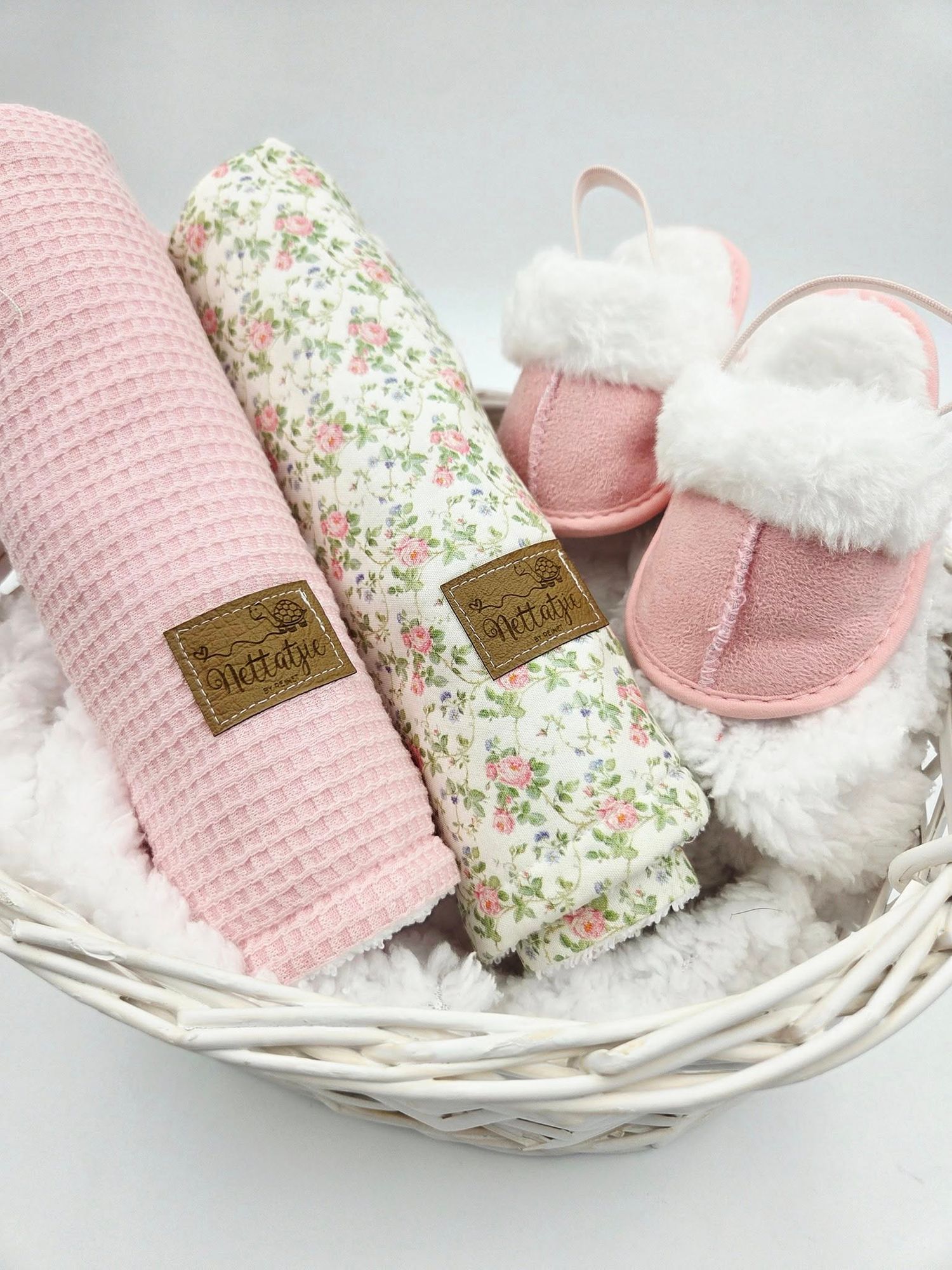 Pink and floral baby blanket collection displayed in white wicker basket with matching shoes.