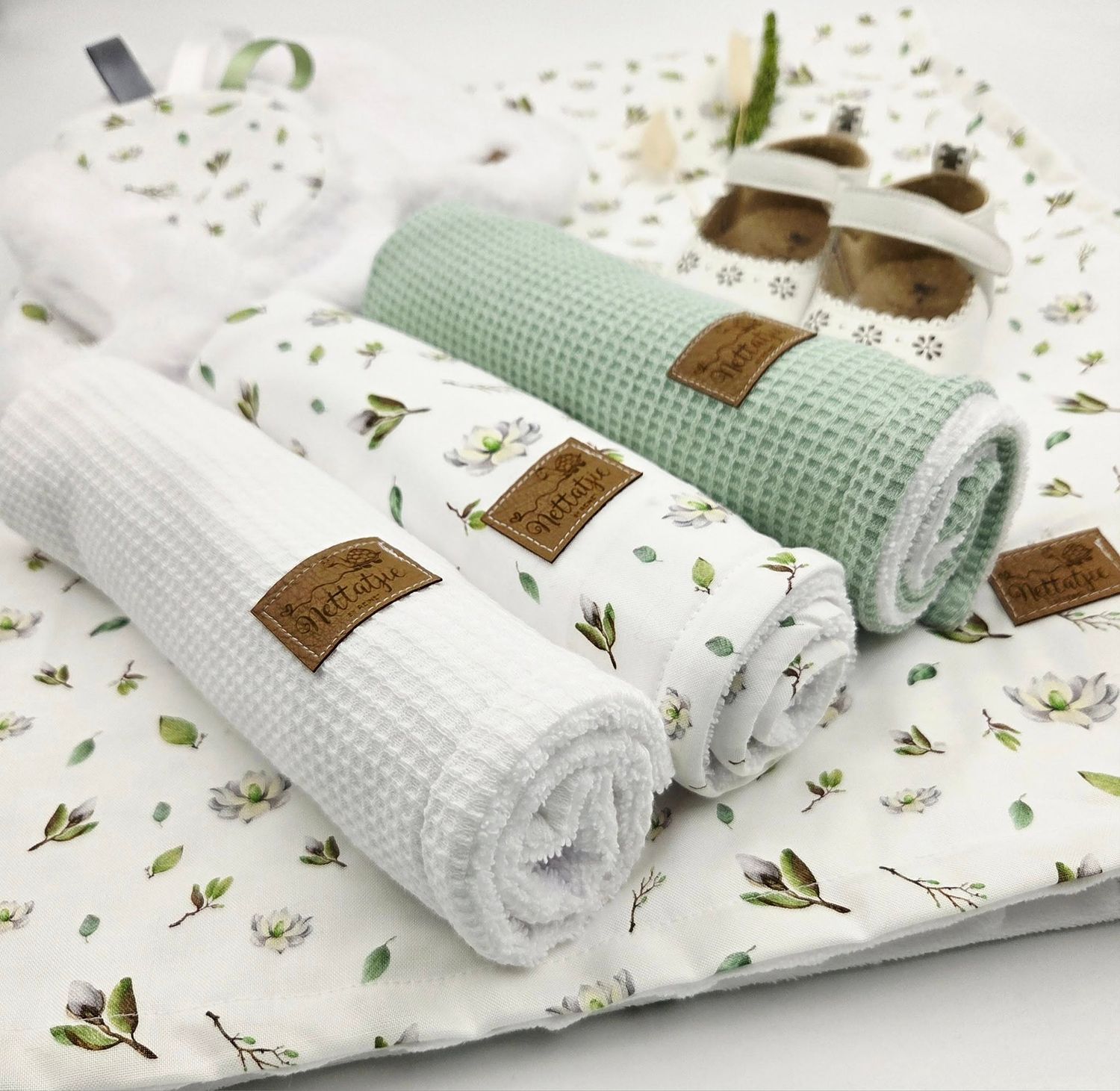 Collection of white and mint green baby textiles with delicate floral patterns and waffle textures.