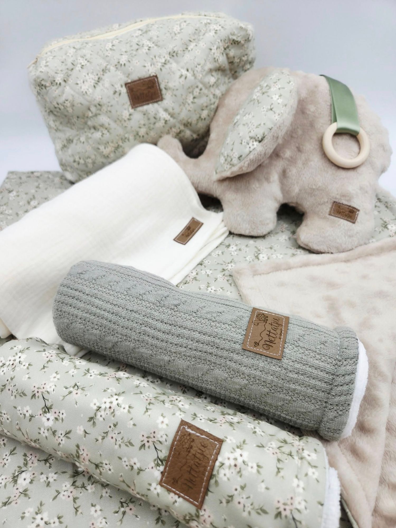 Soft gray knitted blanket with leather tag shown folded with matching accessories on floral background.