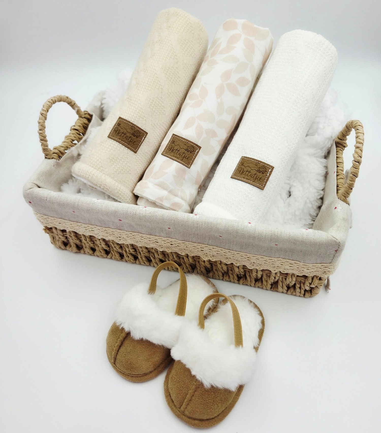 Cream colored baby textiles arranged in woven basket with rope handles.