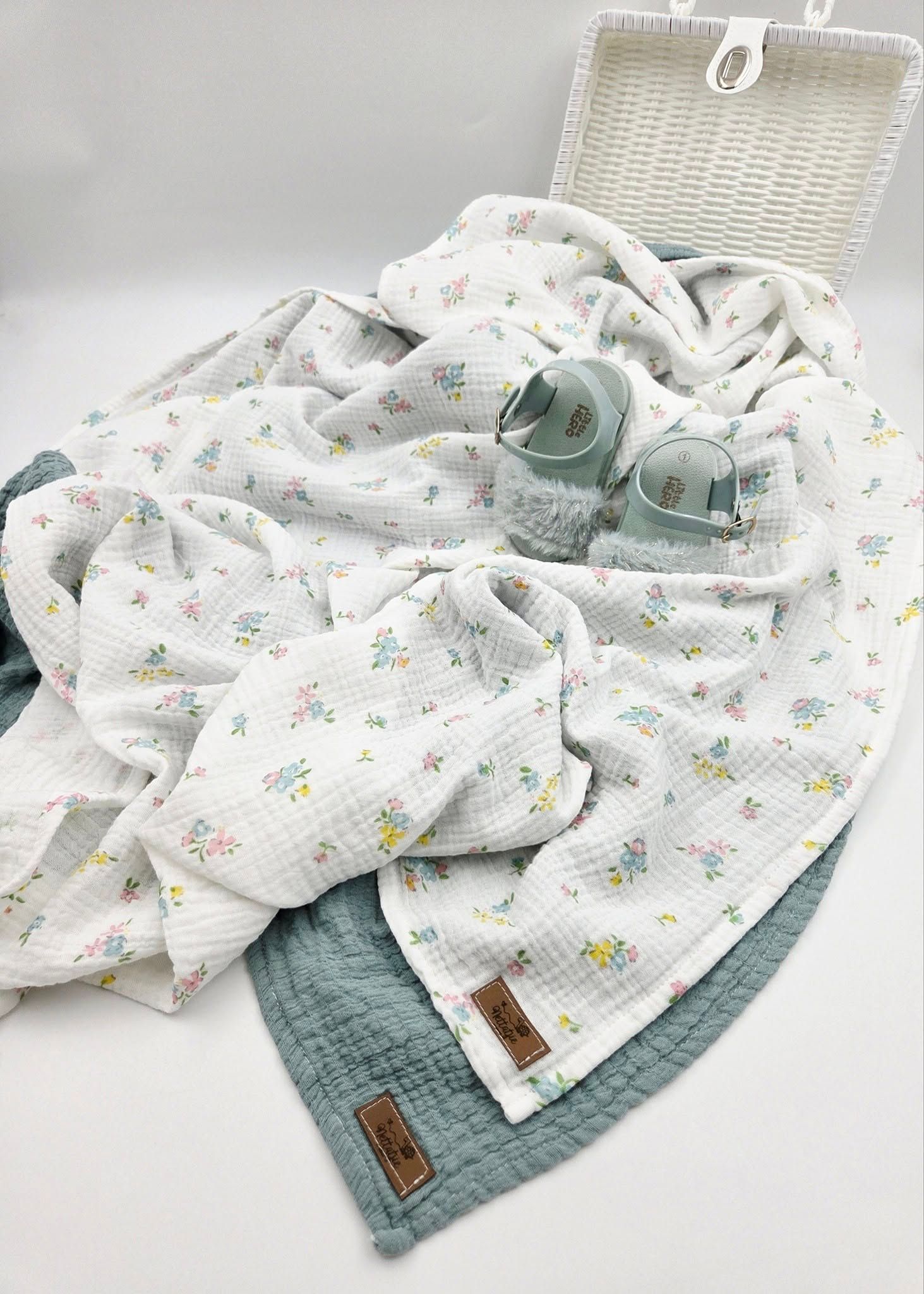 White floral muslin baby blanket with sage green accent and matching mint shoes.