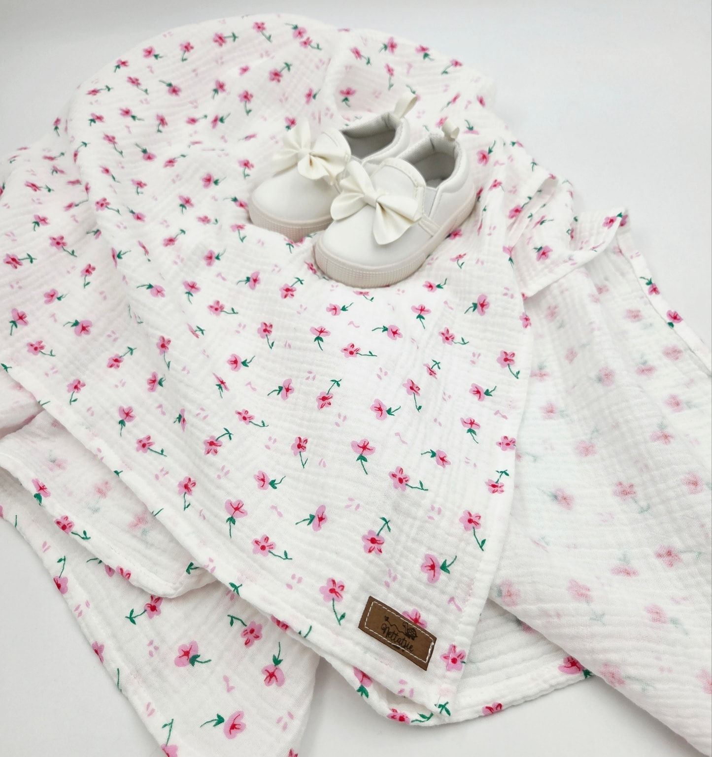 White muslin baby blanket with delicate pink floral pattern and white bow shoes.