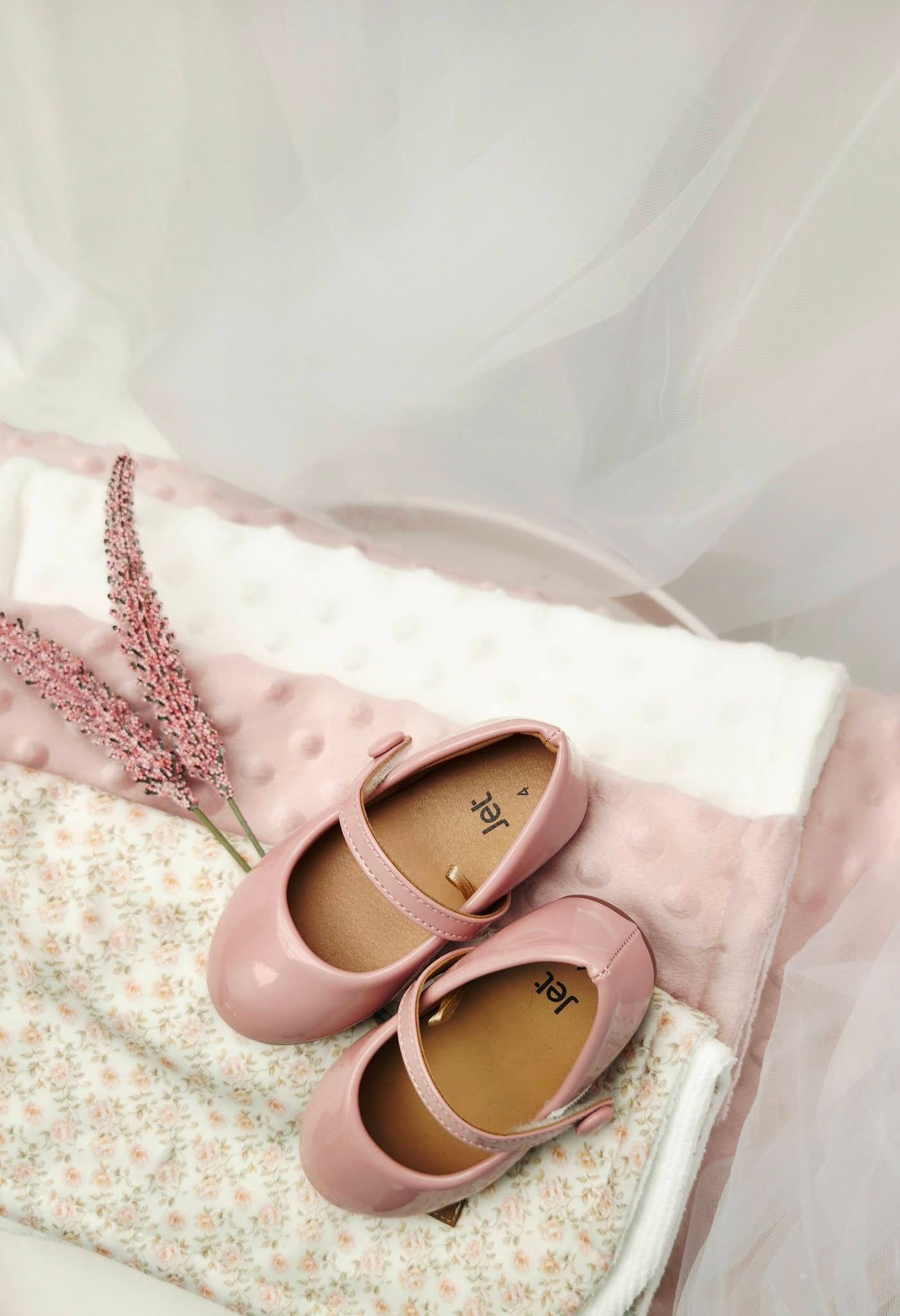 Pink patent leather Mary Jane shoes for girls displayed on a floral blanket with soft pink decor.