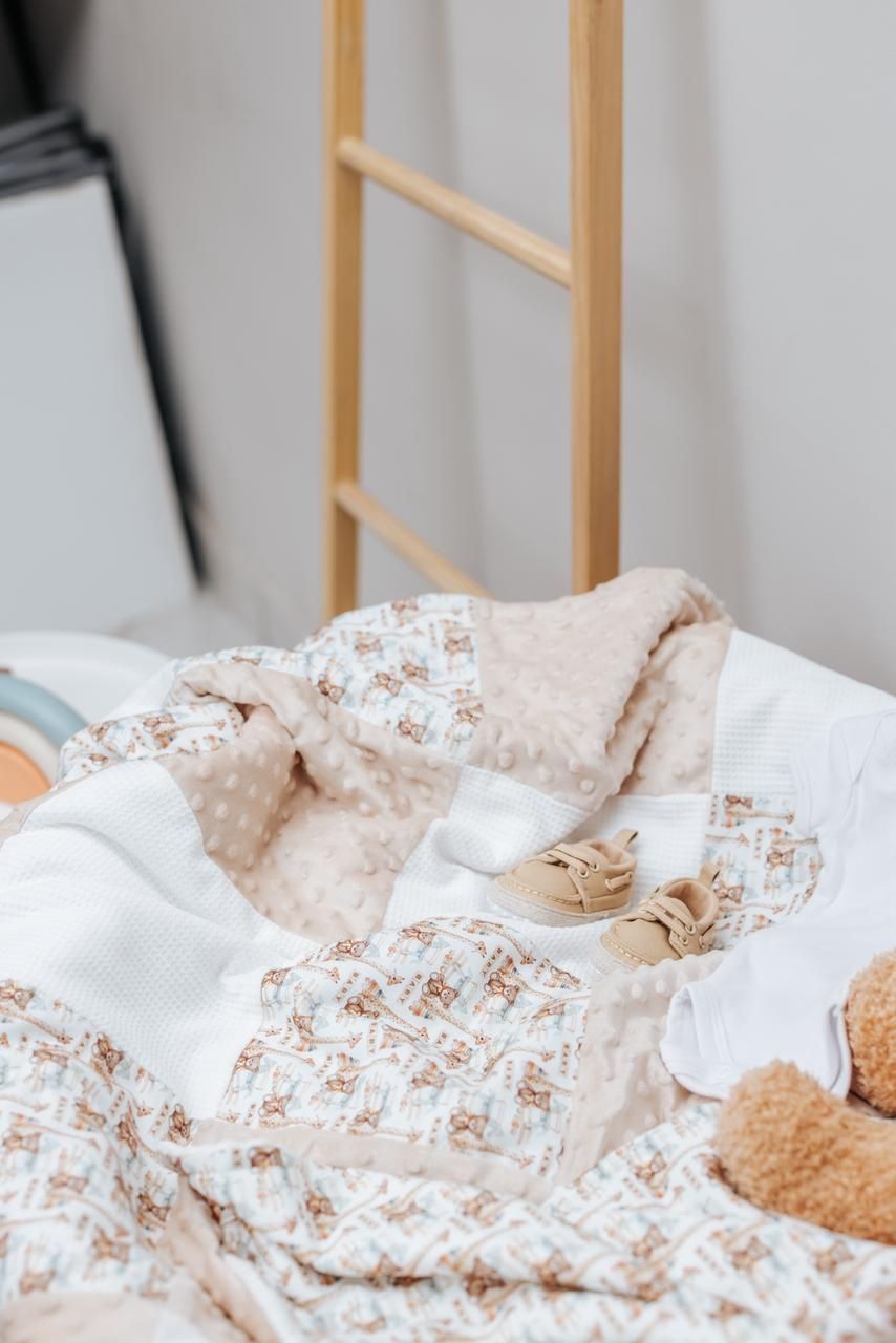 Cozy beige and white patterned baby blanket folded neatly on wooden furniture.