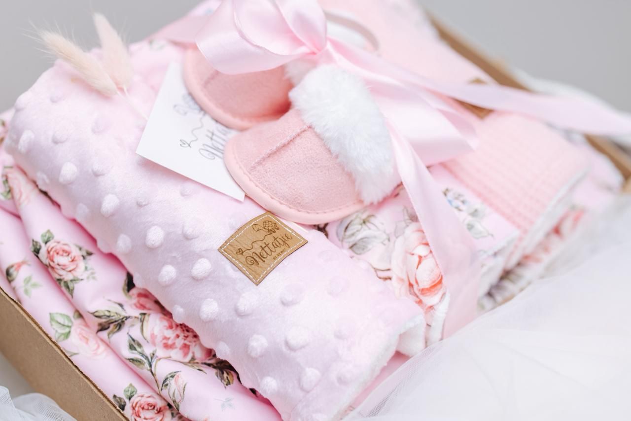 Pink polka dot and floral baby blankets with golden tags arranged in soft layers.