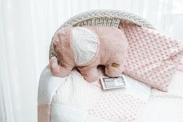 Pink elephant stuffed animal toy resting in a white wicker bassinet with soft pink polka dot blanket.