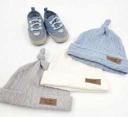 Three knit baby beanies in gray, white, and blue with a pair of blue baby sneakers on a white background.