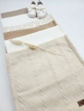 Soft ivory knit baby blanket with lace trim detail, displayed flat with white baby shoes on top.