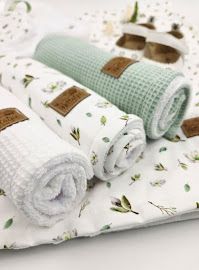 Soft baby muslin blankets and waffle towels in sage green and white floral print, neatly rolled and stacked.