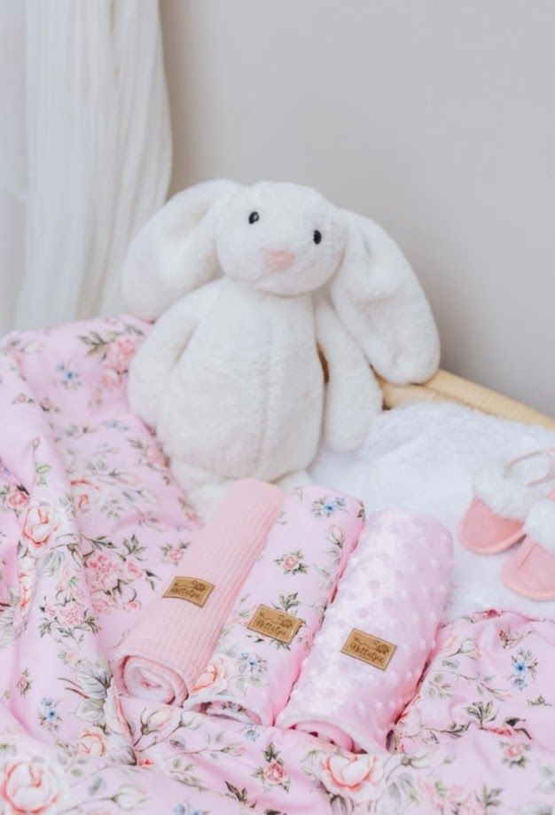 White plush bunny toy beside pink floral baby blankets and accessories on a soft nursery bed.