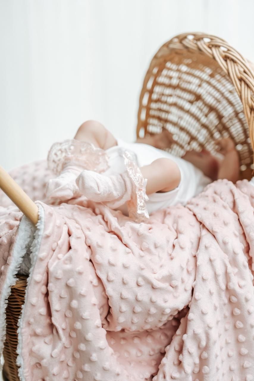 Baby wrapped in soft pink minky dot blanket rests on white background.