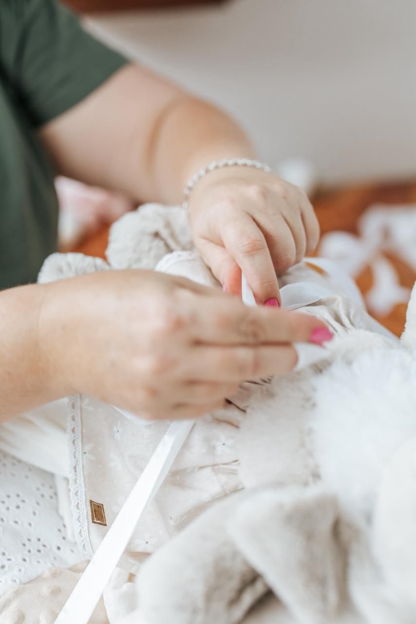Hands carefully arranging and working with delicate white lace fabric and sewing materials on a light surface.