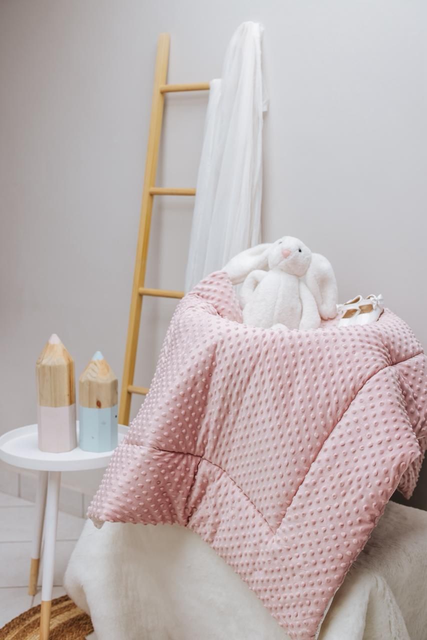 Pink textured baby blanket with wooden ladder and white candles in nursery setting.
