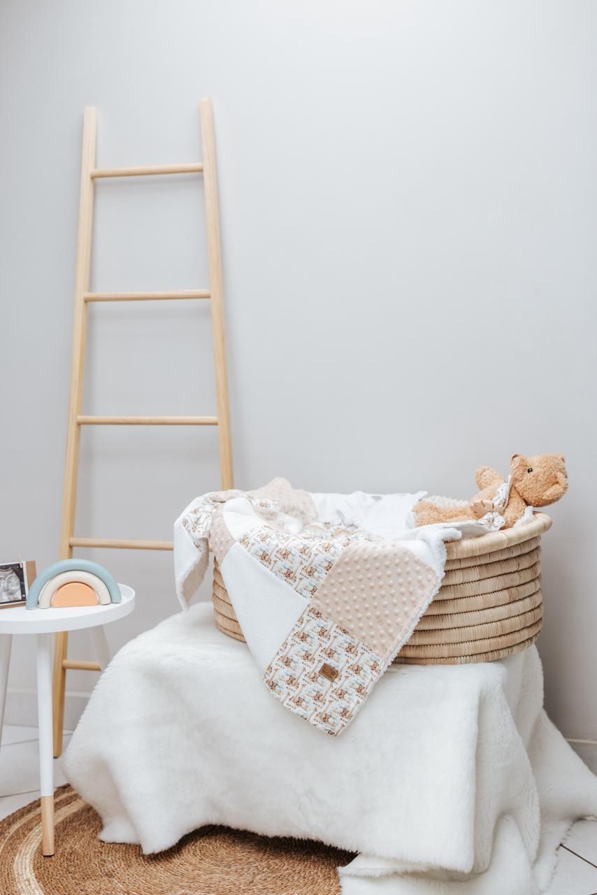 Wooden ladder display with white textured blankets and decorative cushions in a minimalist nursery setting.