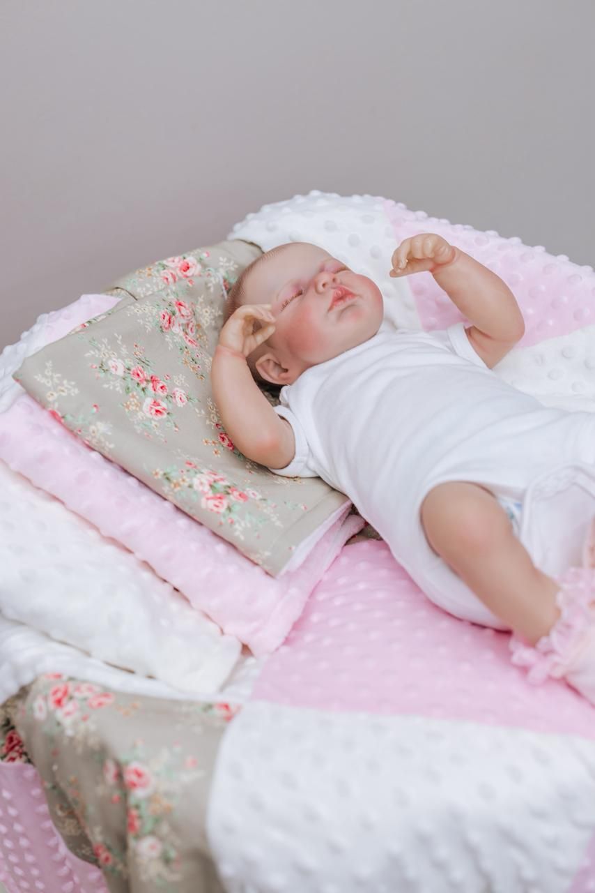 Baby bedding set in soft pink and white with floral accents and plush textures.