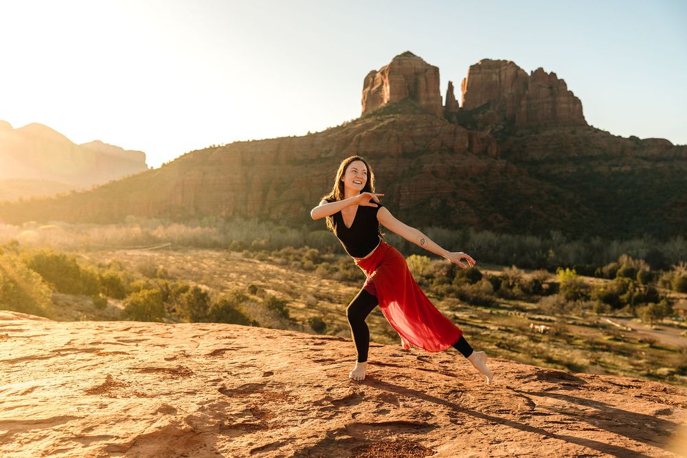 Woman dancing in red skirt on red rocks at sunset with Sedona Arizona red rock buttes in background.