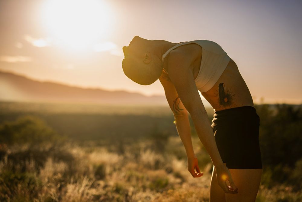 Figure silhouetted against golden sunset bending forward in natural outdoor setting.