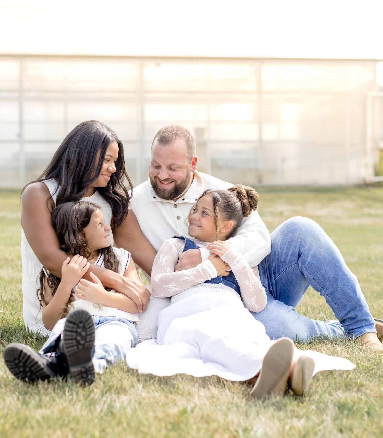 A family dressed in white shares tender moments while relaxing on grass during sunset.