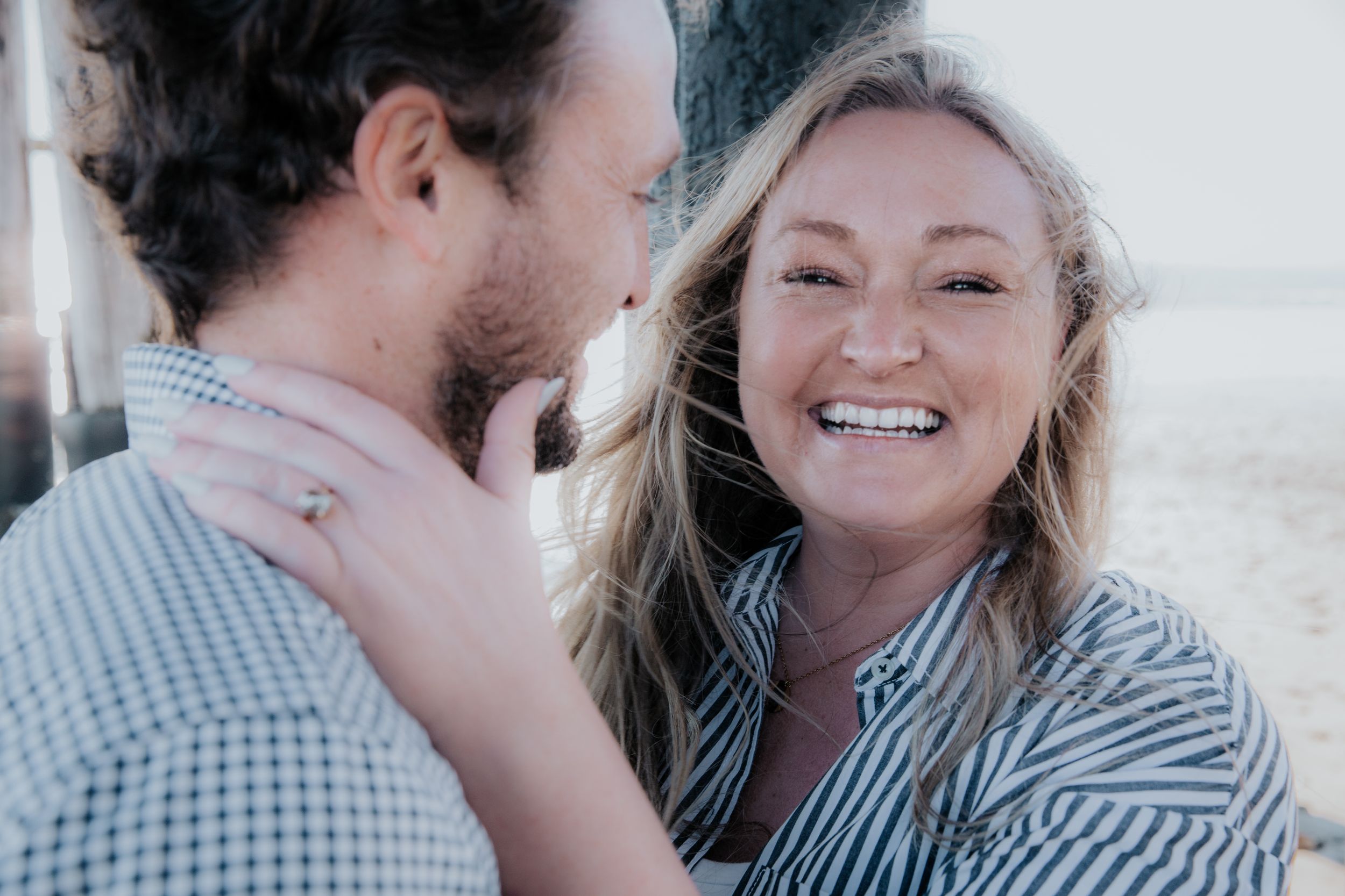 A candid moment between a couple wearing striped button-down shirts sharing laughter outdoors.