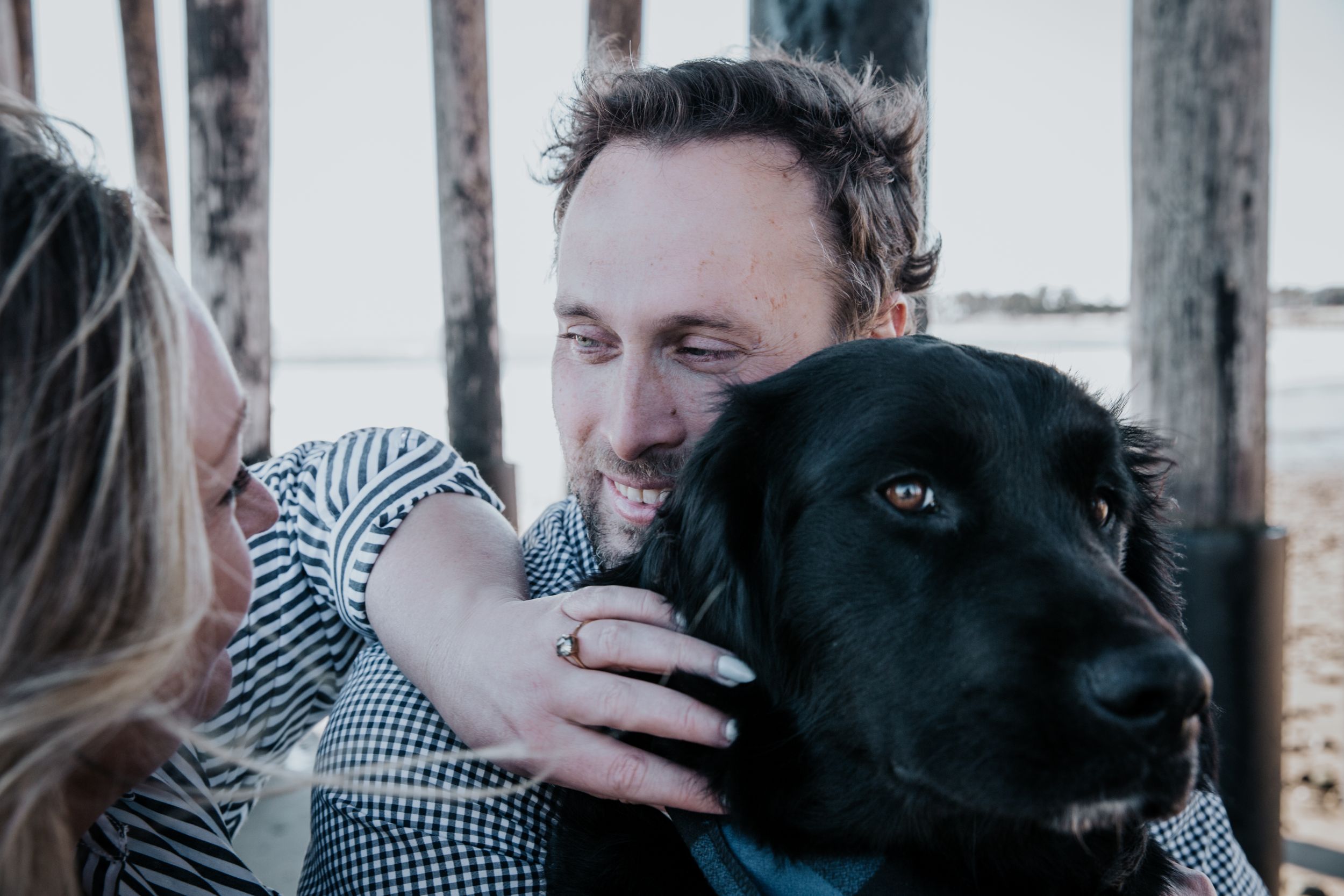 A beautiful black Labrador sits close to two people enjoying an affectionate outdoor moment together.
