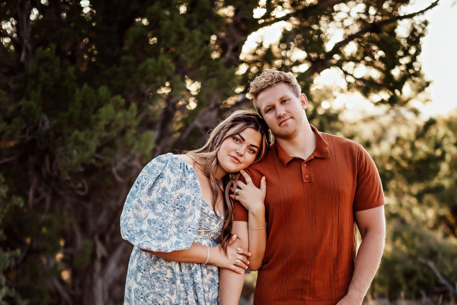 A couple poses together at sunset, wearing casual clothing against a natural backdrop.